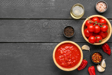 Bowls with tasty tomato sauce and ingredients on dark wooden background