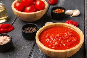 Bowl with tasty tomato sauce on dark wooden background