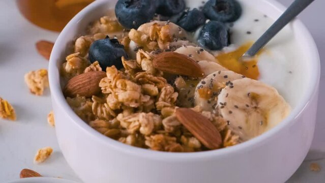 Bowl of greek yogurt with oat granola banana, blueberries, chia seeds, honey and nuts on white background for healthy breakfast Generative AI