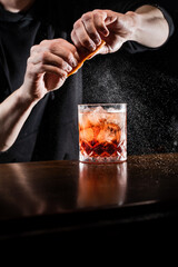 Bartender squeezes orange peel and sprinkles juice over the Negroni in the glass. Bartender...