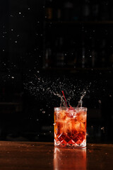 Cherry falling and splashing into Negroni alcoholic cocktail. Bartender prepares classical Negroni cocktail at the bar.
