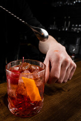 Bartender puts a drop of Negroni alcoholic cocktail on his hand and tastes it. Barman prepares classical Negroni cocktail at the bar.