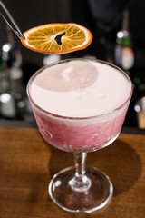 Bartender is decorating pink Clover club alcoholic cocktail with orange slice at the bar. Bartender mixes egg white, lemon, dry vermouth and gin to prepare the Clover club cocktail.