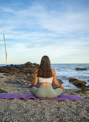 Woman on her back meditating sitting on a mat doing yoga in lotus posture and looking at the sea at...
