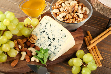 Board with tasty cheese, nuts and grapes on wooden background