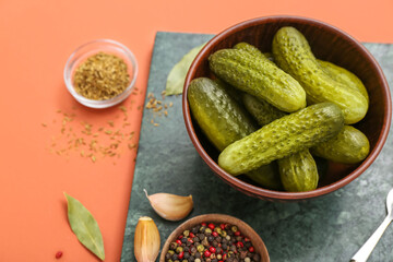 Board with bowl of tasty canned cucumbers and ingredients on red background