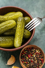 Bowl of tasty canned cucumbers and peppercorns on grunge background