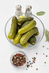 Bowl of tasty canned cucumbers with spices on white background
