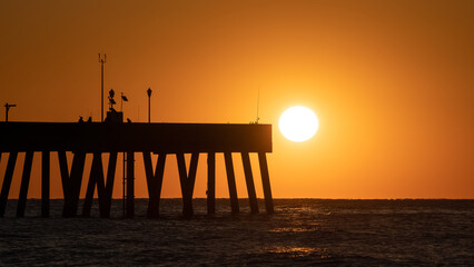Sun rising in the ocean with the Johnnie Mercers Fishing Pier on the left side.
