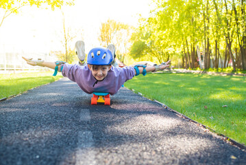a boy rides on a skateboard lying on his stomach, a child in a purple helmet and protection on his...
