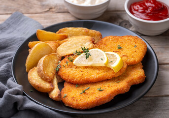 Chicken schnitzel with sauce, fried potatoes and lemon in a plate