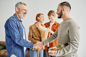 pleased father shaking hands with gay man near mother and son with flowers at home. 