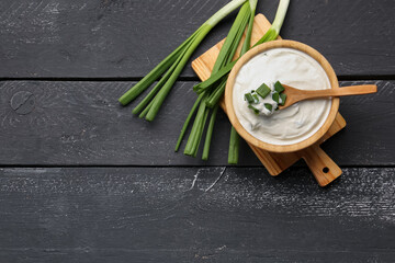 Bowl of tasty sour cream with green onion on dark wooden background