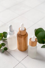 Fototapeta na wymiar Bottles of cosmetic oil and eucalyptus branches on white tile