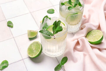 Glasses of tasty mojito and ingredients on white tile background