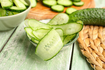 Bowl with slices of fresh cucumber on light wooden background