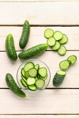 Bowl with fresh cut cucumbers on light wooden background