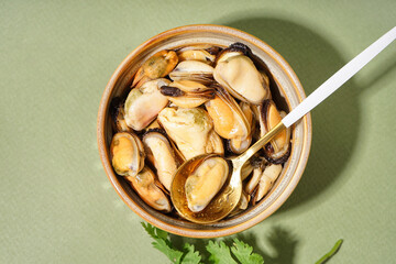 Bowl with pickled mussels on green background