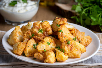 Fried in batter Cauliflower florets served on a black plate on a grey concrete table with ingredients, view from above, close-up, flatlay, copy space (Turkish name; karnabahar kizartmasi)