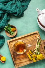 Board with glass cup of healthy dandelion tea and teapot on green background