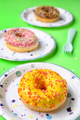 Paper disposable plates with donuts on green background, closeup