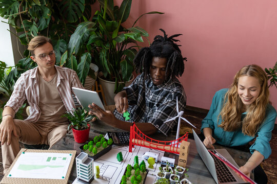 Diverse group of international students working on the urban project of modern city with renewable energy source, green areas. Concept of ecology, environment protection, waste recycling, technology