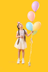 Little girl in crown with balloons on yellow background. Children's Day celebration