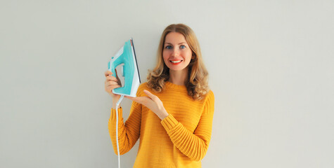 Household chores, ironing - happy smiling woman housewife holding an iron in her hands on gray wall...