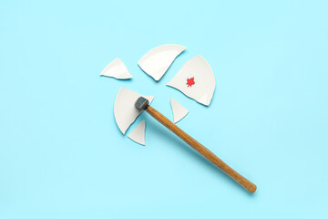 Hammer and broken plate with paper maple leaf on blue background. Canadian flag concept
