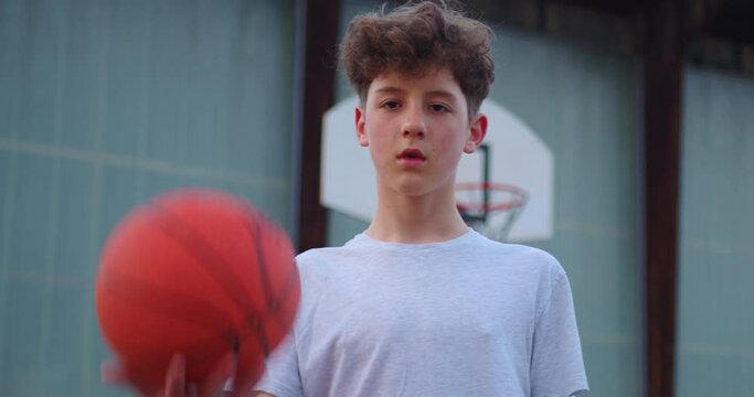 Video of a boy standing on a basketball court and holding a basketball. Cinematic shot of teenager standing with a ball in his hand and a basketball basket behind him Generative AI