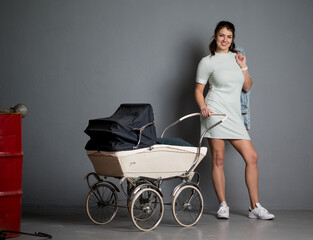 Hübsche junge braunhaarige Frau mit Kinderwagen und Jeansjacke  im Studio