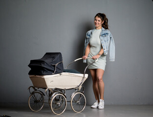 Hübsche junge braunhaarige Frau mit Kinderwagen und Jeansjacke  im Studio