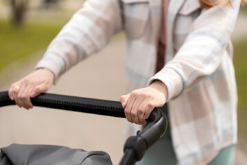 Closeup, young woman pushing baby carriage, selective focus. Walking with baby outdoors