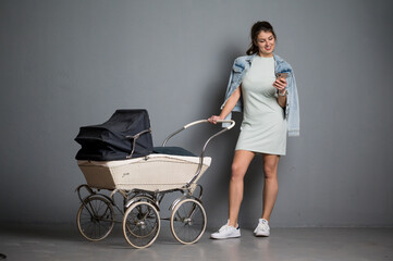 Hübsche junge braunhaarige Frau mit Kinderwagen und Jeansjacke mit Handy in der Hand