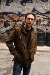 Fototapeta na wymiar Bearded caucasian man with brown jacket posing in front of a graffiti wall