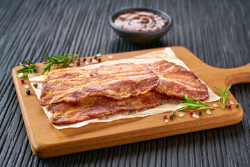 fried bacon strips and bbq sauce on a black table, selective focus.