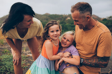 family hugging and smiling at the camera at the beach with mountains and greenery behind them