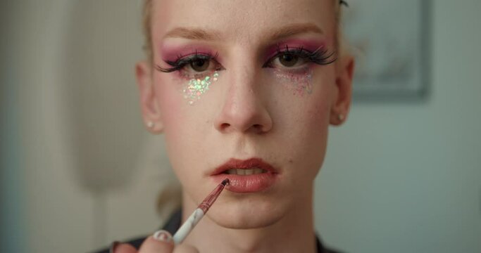 Transgender guy app;ying lipstick and using little mirror