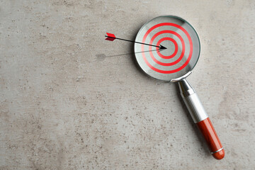 Magnifying glass with illustration of target and arrow on grey textured background, top view. Space...