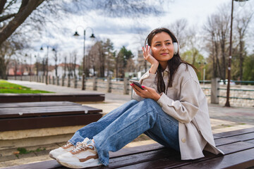 One young girl is listening to music on her wireless headphones and using her phone outdoors	
