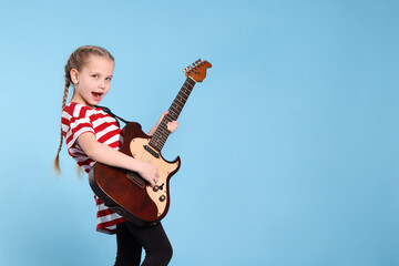 Fototapeta premium Cute girl with electric guitar on light blue background. Space for text