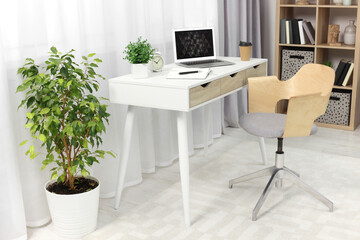 Workplace with modern laptop on desk and comfortable chair at home