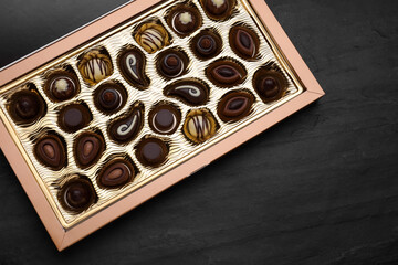 Box of delicious chocolate candies on black table, top view. Space for text