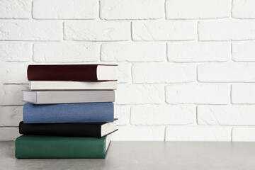 Stack of hardcover books on grey table near white brick wall, space for text