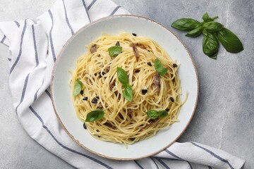 Delicious pasta with anchovies, olives and basil on light grey table, flat lay
