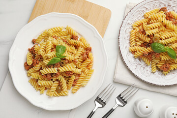 Delicious pasta with minced meat and basil served on white table, flat lay