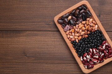 Plate with different kinds of dry kidney beans on wooden table, top view. Space for text