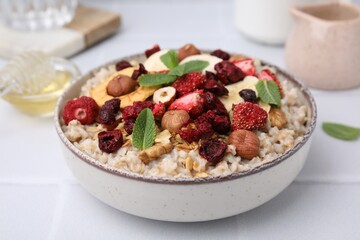 Oatmeal with freeze dried fruits, nuts and mint on white wooden table, closeup