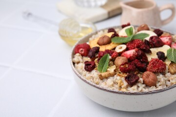 Oatmeal with freeze dried fruits, nuts and mint on white wooden table, closeup. Space for text