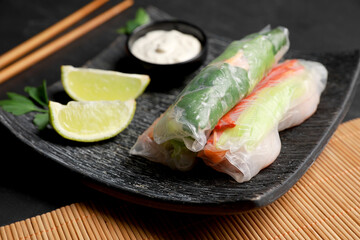 Delicious rolls wrapped in rice paper served on black table, closeup